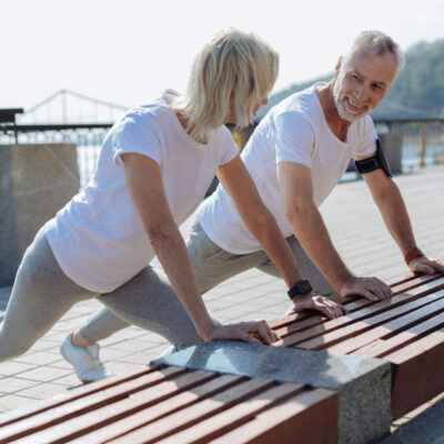 Middle-aged couple stretching their calf muscles on a park bench.