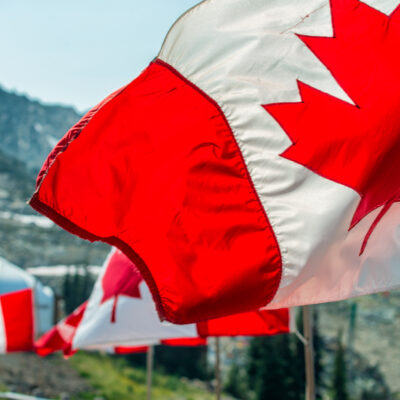 Canada flags waving at the wind in mountain scenario.