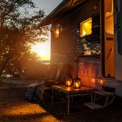 Road Trip Adventures. Calm Warm Night on a Camping. Camper Van, Outdoor Chairs and Romantic Light From Lanterns. Vacation in Recreational Vehicle.