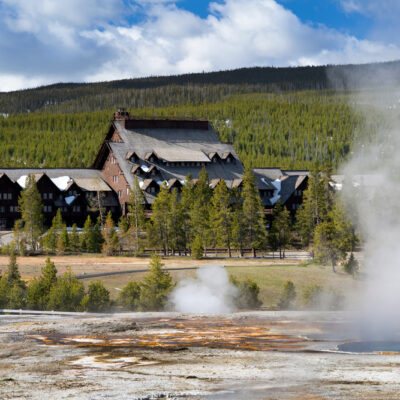 Old Faithful Inn with geysers and steam in foreground.