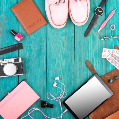 Travel Products- shoes, tablet pc, passport, camera, notepad, watch, headphones and essentials on blue wooden desk