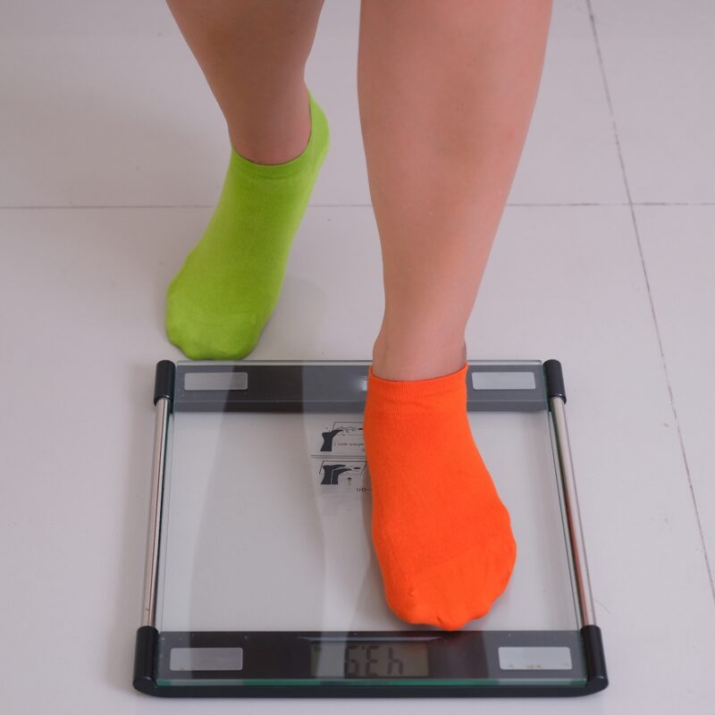 Pair of female legs on multi-colour socks stepping on electronic scale