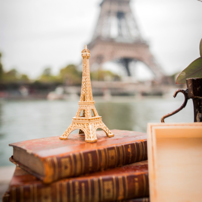 Small decorative Eiffel Tower standing on a vintage books under the real Eiffel Tower in Paris.